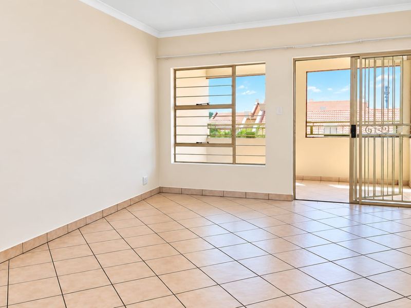 A bright, empty living room featuring tiled floors, a sliding glass door with a security gate, and access to an outdoor balcony area.