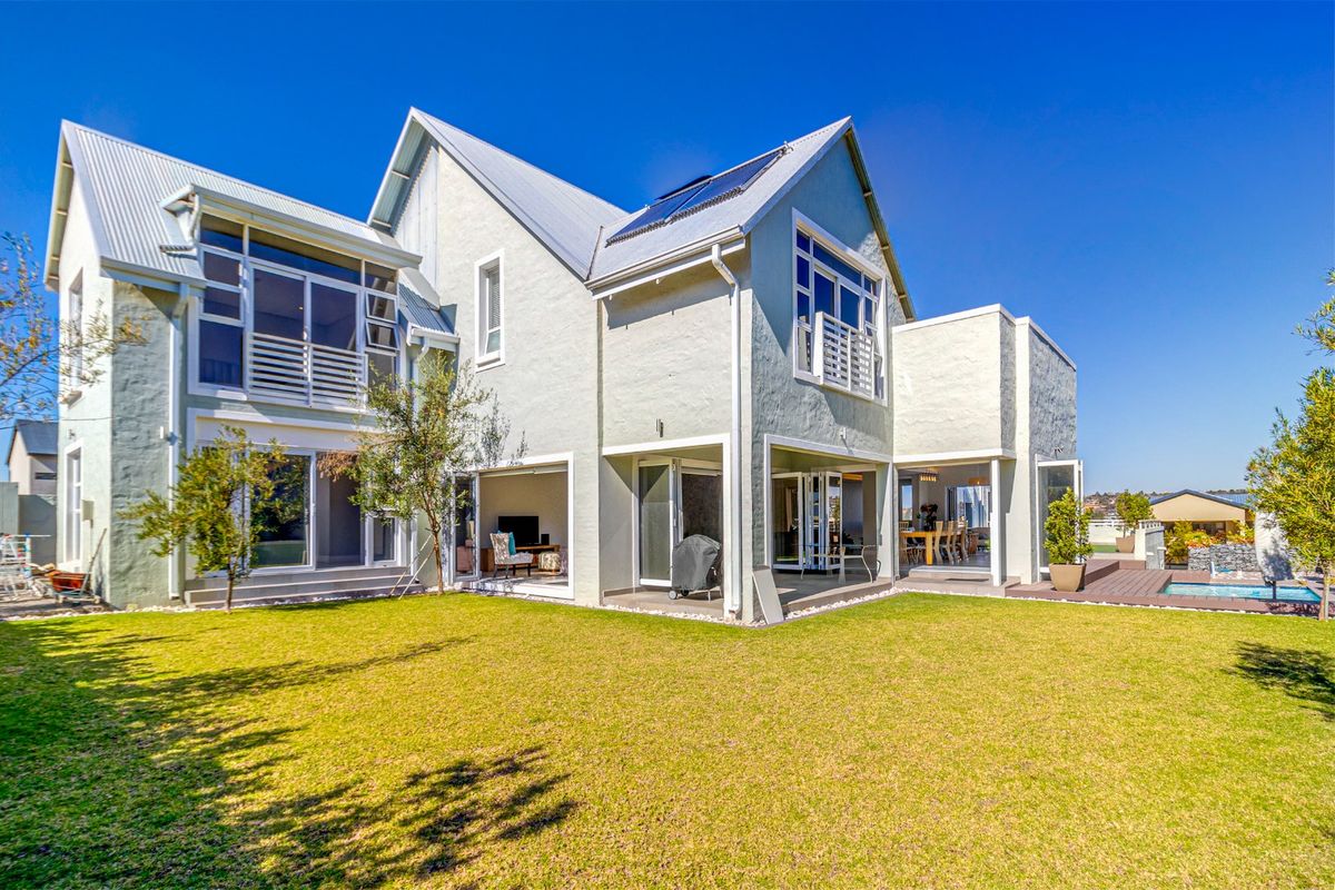 A well-maintained rear elevation featuring a spacious lawn, covered patio, integrated decking, and a swimming pool, showcasing modern architectural design and seamless indoor-outdoor flow.