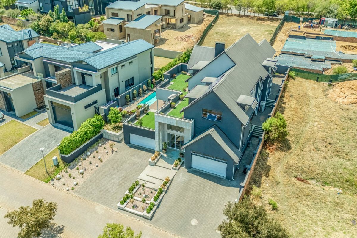 Aerial view of a modern multi-story residential property featuring a paved driveway, double garage, and an elevated roof terrace with a swimming pool.