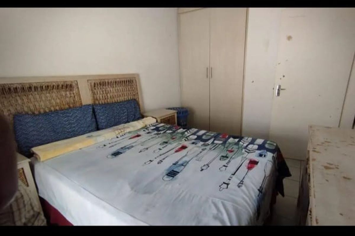 A bedroom featuring built-in cupboards and tiled flooring, currently showing signs of wear on the walls and doors.