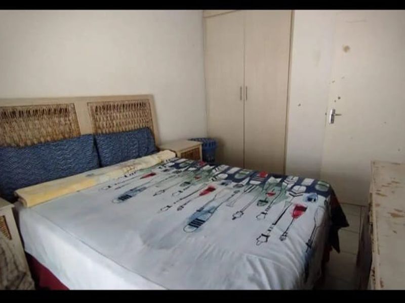 A bedroom featuring built-in cupboards and tiled flooring, currently showing signs of wear on the walls and doors.