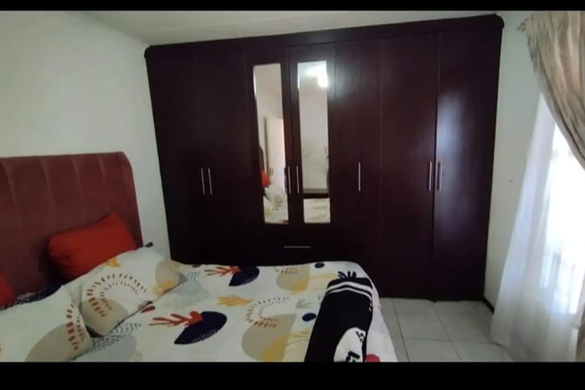 A bedroom featuring dark wood built-in cupboards with integrated mirrors and tiled flooring.