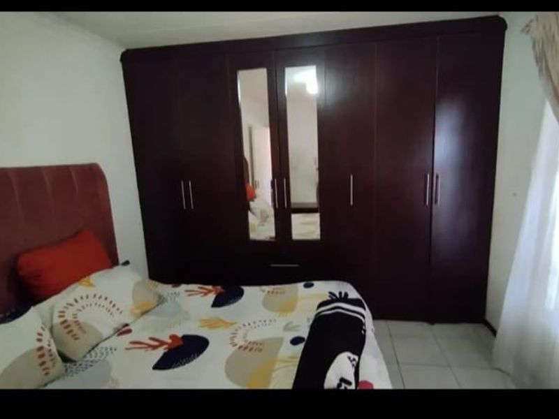 A bedroom featuring dark wood built-in cupboards with integrated mirrors and tiled flooring.
