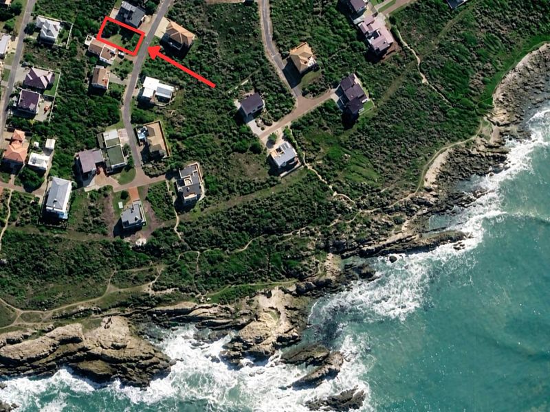 Aerial view of a residential coastal plot highlighted in red, situated in a developed neighborhood near the ocean.