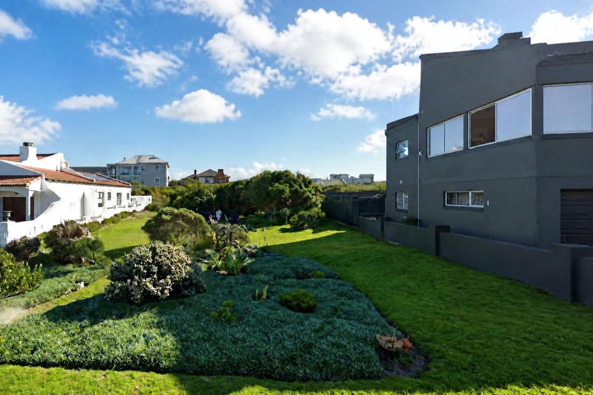 A well-maintained rear garden area featuring a lush lawn and established landscaping, adjacent to the side elevation of a residential property.