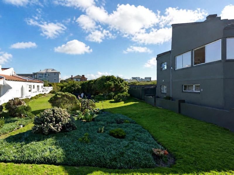 A well-maintained rear garden area featuring a lush lawn and established landscaping, adjacent to the side elevation of a residential property.