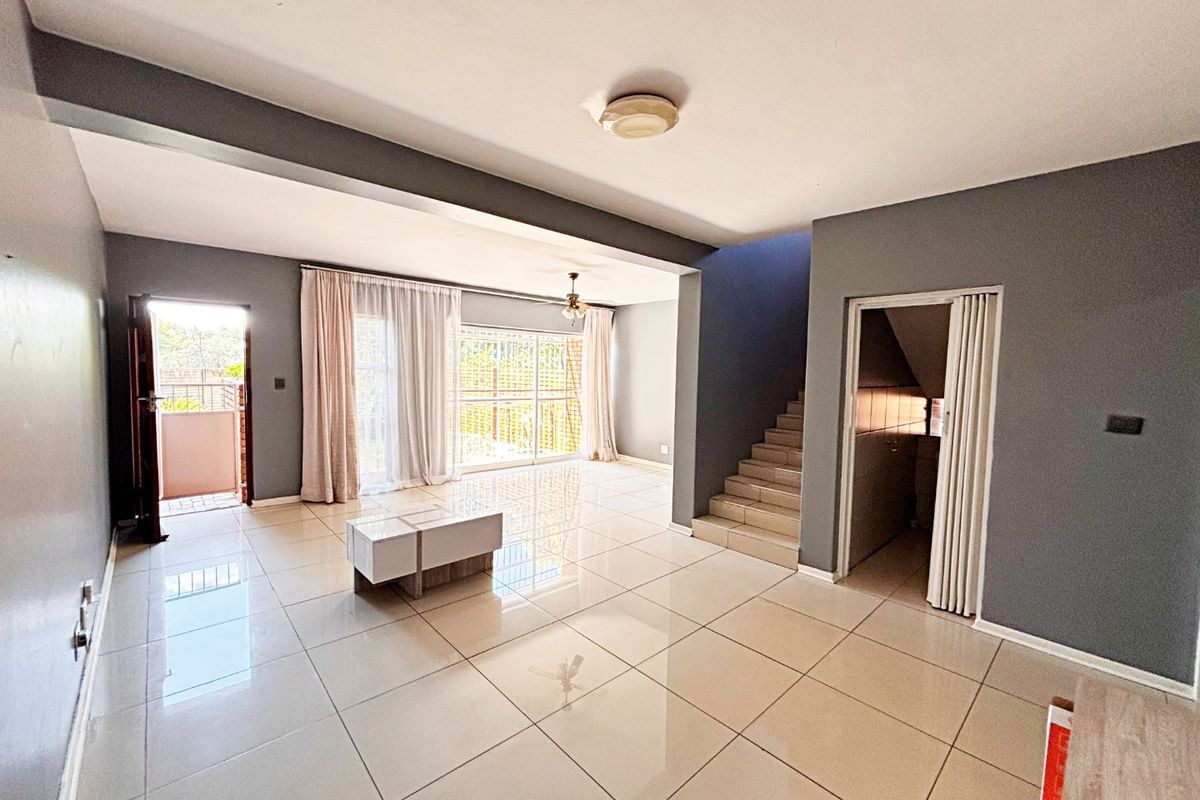 Spacious open-plan living area featuring large format floor tiles, a staircase, and sliding glass doors leading to an outdoor space.