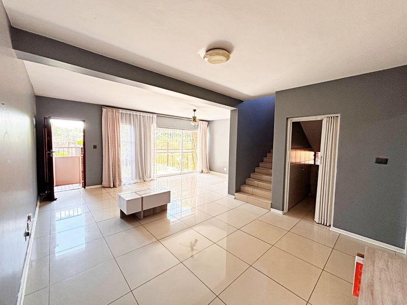 Spacious open-plan living area featuring large format floor tiles, a staircase, and sliding glass doors leading to an outdoor space.
