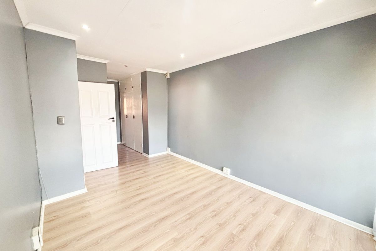 A bright, empty bedroom featuring light wood-look laminate flooring, grey painted walls, and built-in storage cupboards.