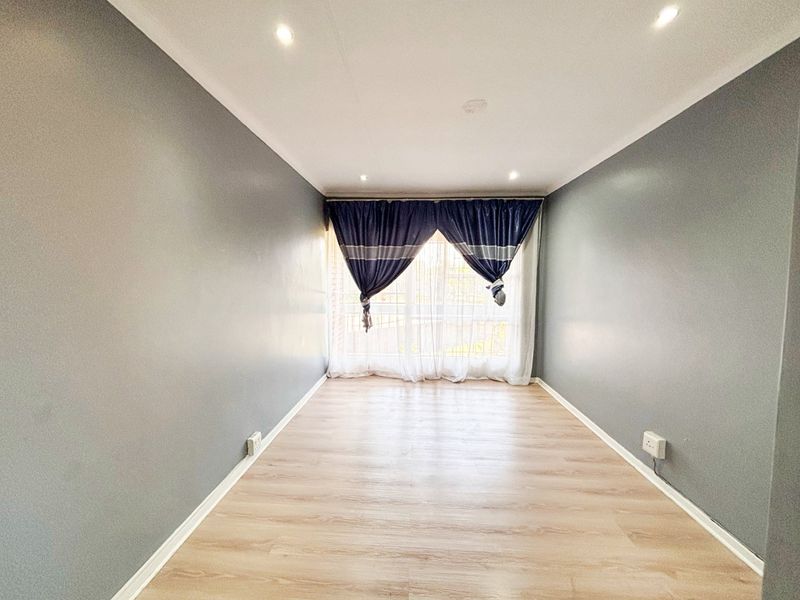 A bright, empty living room featuring light wood-look laminate flooring, grey painted walls, and recessed ceiling downlights.