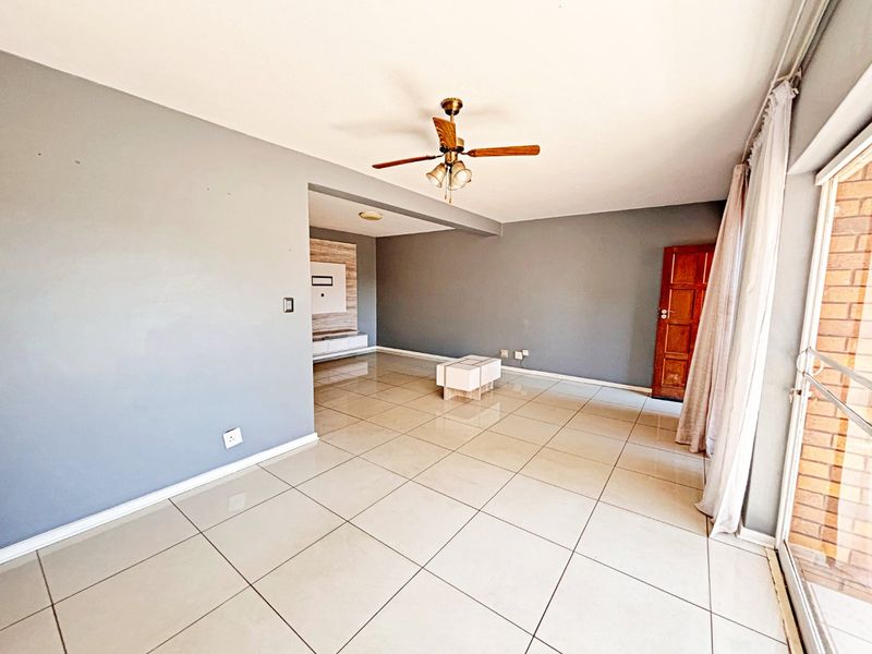 Spacious living area featuring neutral grey walls, large format floor tiles, a ceiling fan, and a built-in media console.