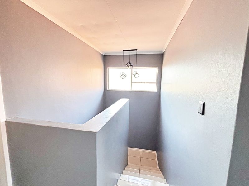 A bright, empty stairwell featuring tiled steps, grey painted walls, and modern pendant lighting, providing a clean transition between levels.