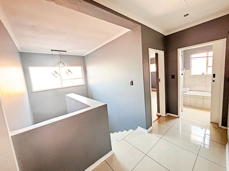 A bright and spacious upper-level hallway featuring neutral grey walls, polished floor tiles, and a staircase balustrade, leading to adjacent rooms.