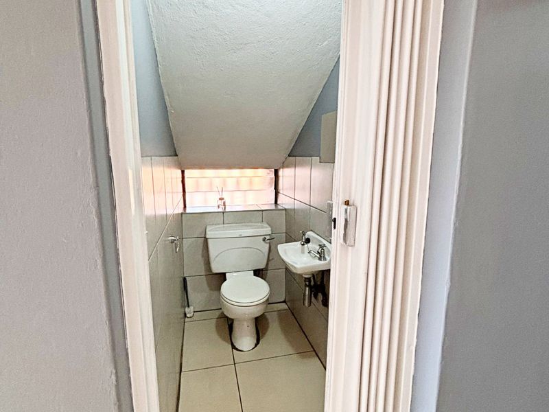 A compact guest bathroom featuring a toilet, wall-mounted basin, and tiled finishes, accessed via a folding door.