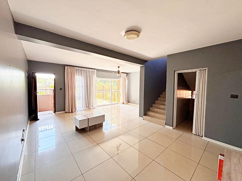 Spacious open-plan living area featuring polished tiled flooring, a staircase, and large sliding glass doors providing access to the exterior.