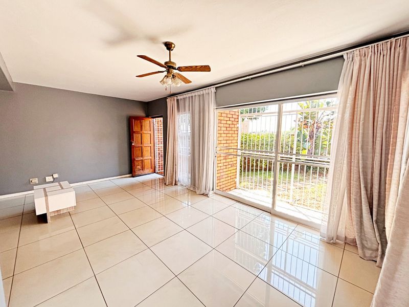 Spacious living area featuring large format floor tiles, a ceiling fan, and sliding glass doors providing direct access to the outdoor garden area.