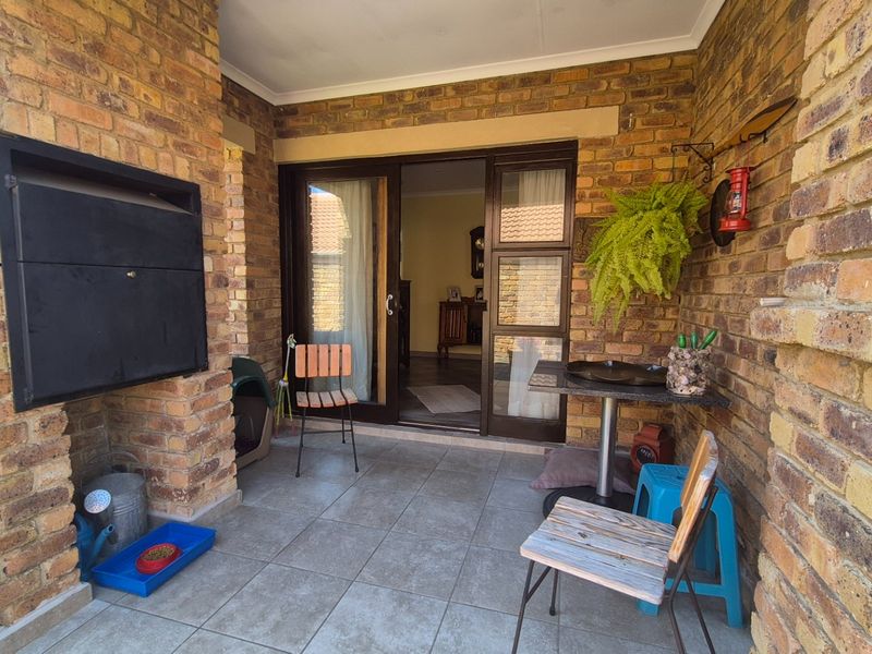 A covered patio area featuring exposed brick walls, tiled flooring, and a built-in fireplace, providing a functional outdoor space for relaxation.