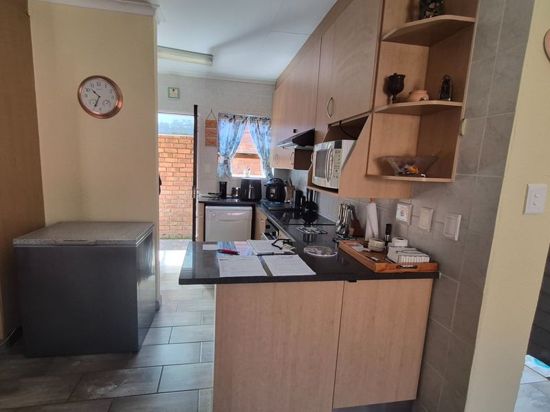 A functional kitchen featuring light wood-tone cabinetry, dark laminate countertops, tiled backsplash, and direct access to an outdoor area.