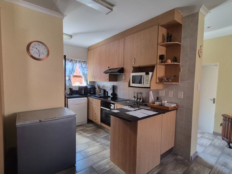 A functional kitchen featuring light wood-tone cabinetry, dark countertops, built-in appliances, and tiled flooring, offering a practical layout for daily meal preparation.
