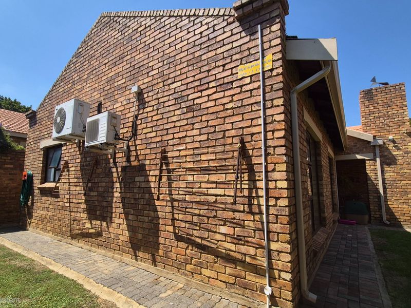 Rear exterior view of the house featuring face brick walls, paved pathways, and wall-mounted air conditioning units.