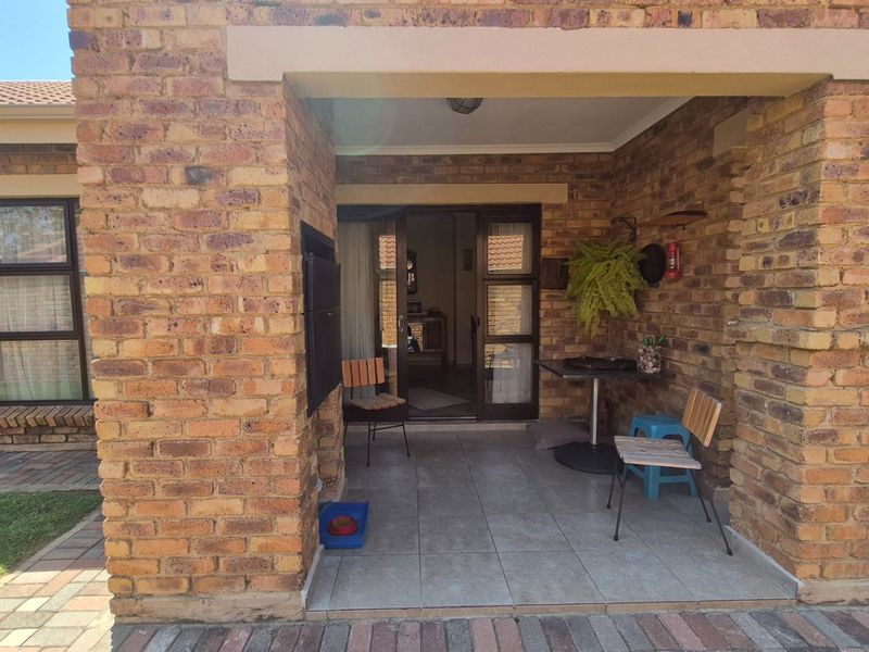 A covered patio area featuring face brick walls, tiled flooring, and a built-in braai, providing a functional outdoor entertainment space.