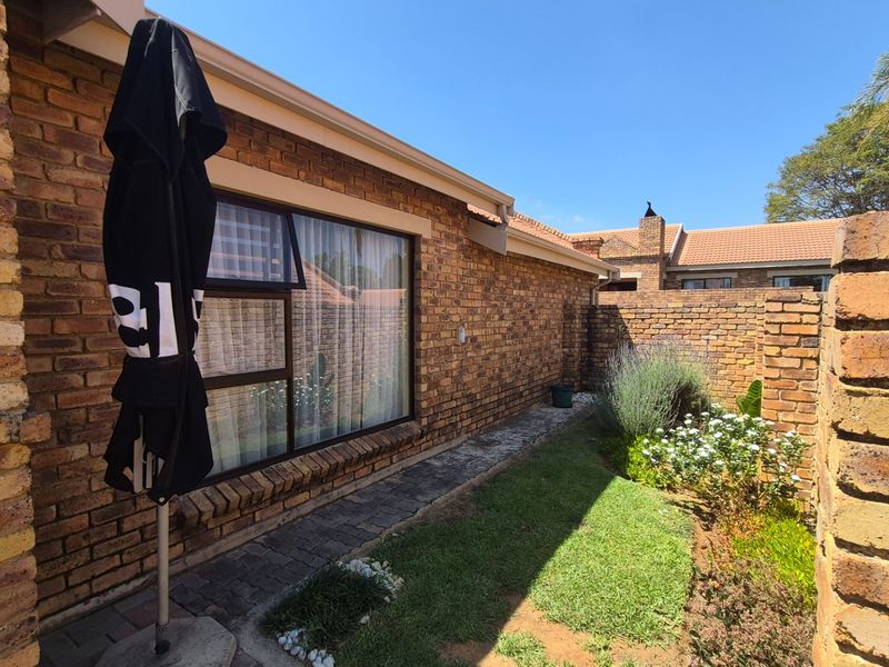 A well-maintained rear exterior view featuring face brick walls, a paved walkway, and a neat garden area with established boundary walls.
