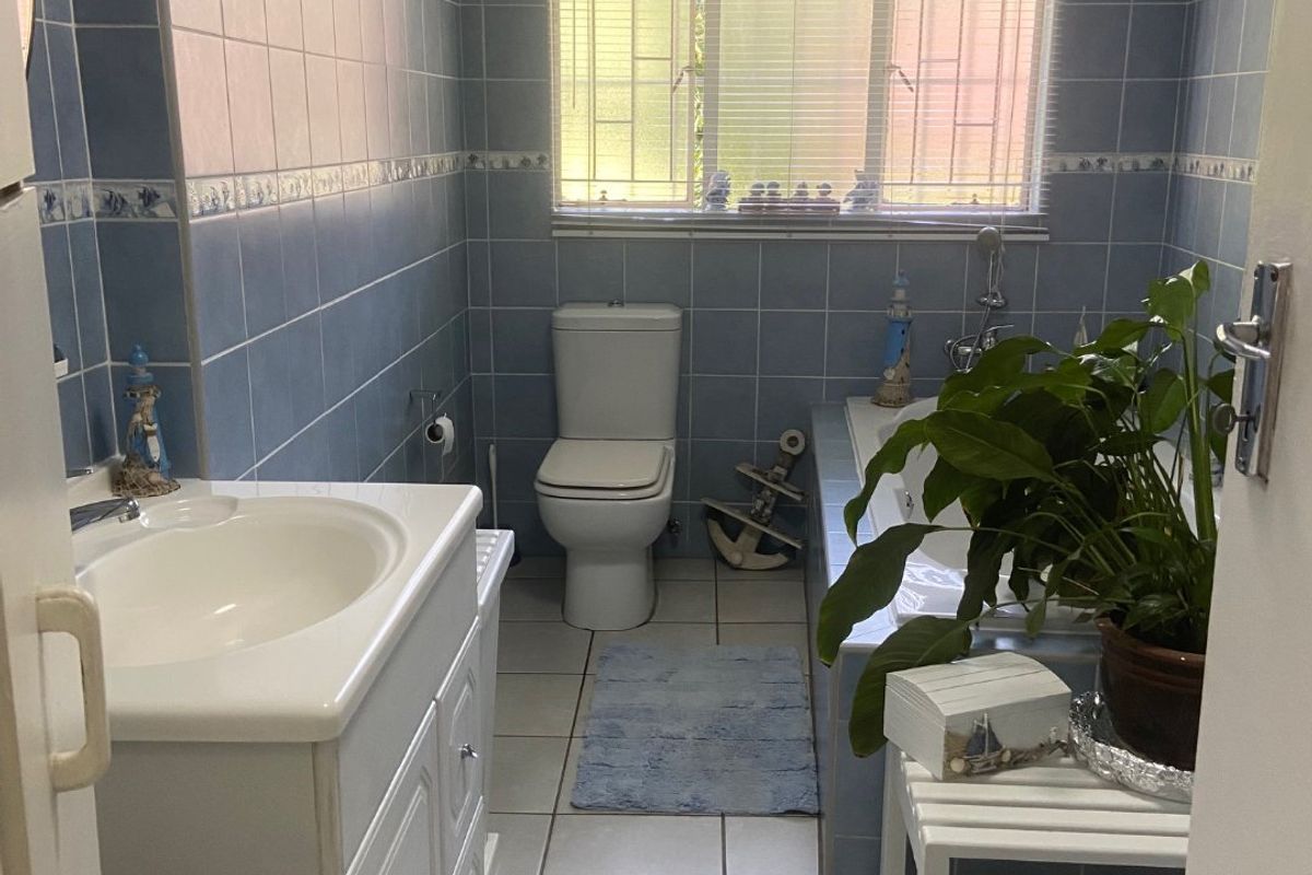 A functional bathroom featuring blue wall tiles, a built-in vanity, a toilet, and a bathtub with a window providing natural light.