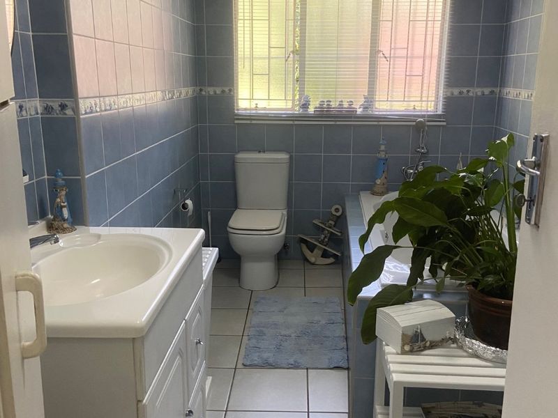 A functional bathroom featuring blue wall tiles, a built-in vanity, a toilet, and a bathtub with a window providing natural light.