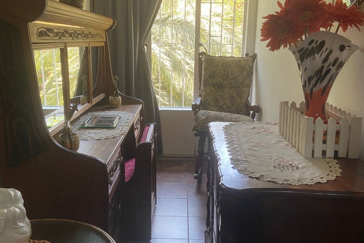 A narrow bedroom featuring tiled flooring and a window with a security gate, offering natural light and a view of the garden.