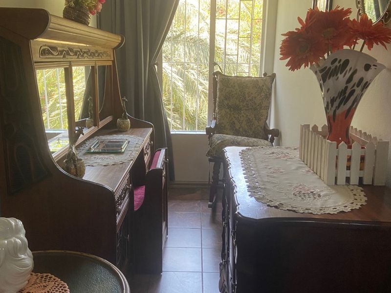 A narrow bedroom featuring tiled flooring and a window with a security gate, offering natural light and a view of the garden.