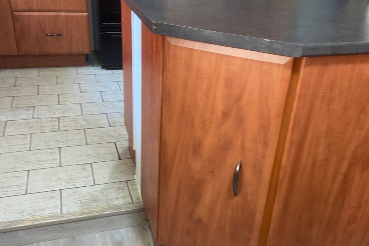 A functional kitchen featuring wooden cabinetry, a central island with a dark countertop, and a tiled backsplash with a freestanding stove.