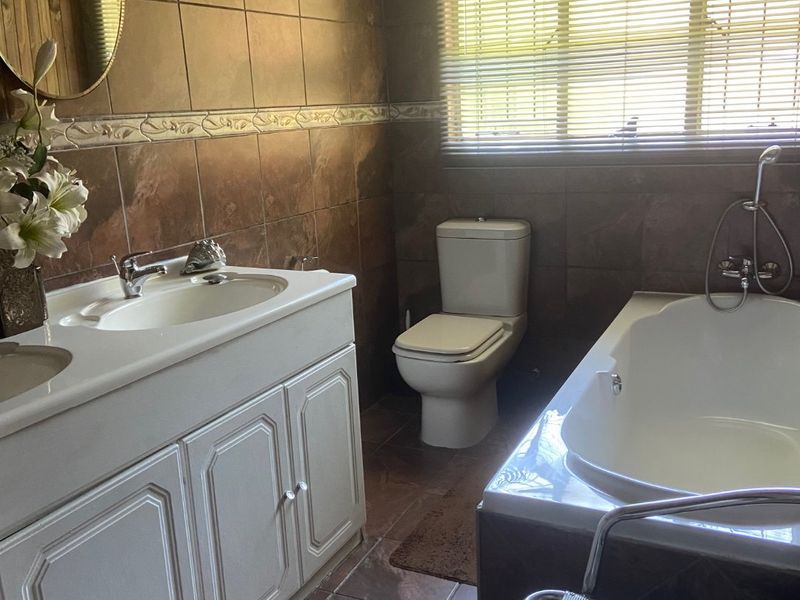 A functional bathroom featuring a double vanity, toilet, and bathtub with brown tiled walls and flooring.