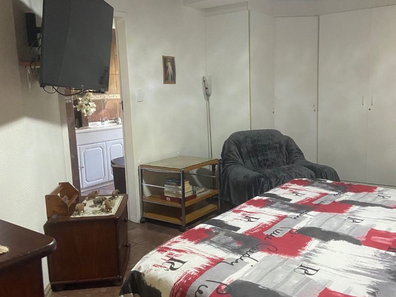 A bedroom featuring built-in cupboards, tiled flooring, and a timber ceiling, with an adjacent view into a bathroom area.