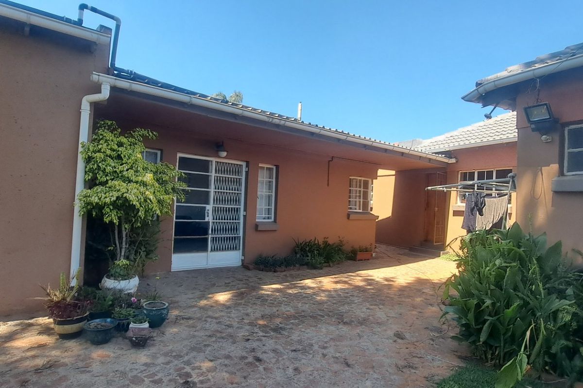 A rear courtyard area featuring paved flooring, security gates, and access to the main dwelling structure.