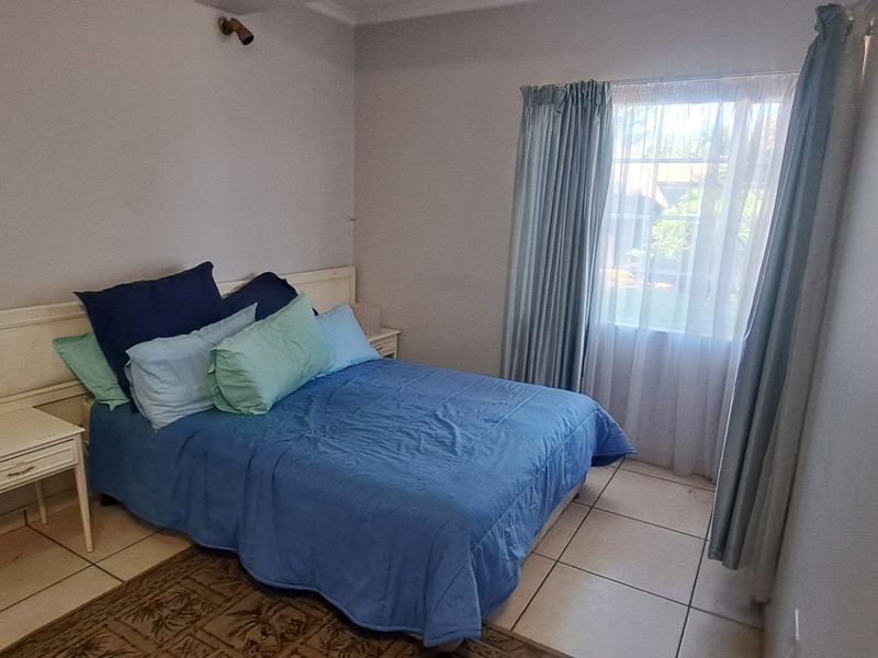 A bedroom featuring tiled flooring, a built-in headboard, and a window with curtains, offering a functional and neutral living space.