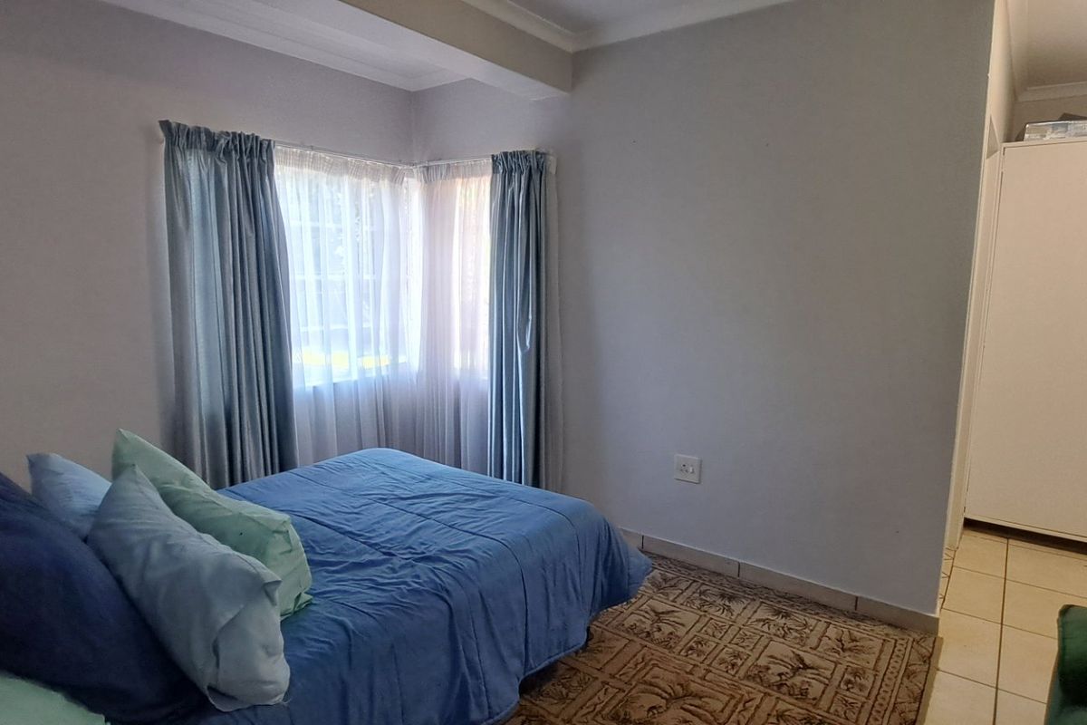 A functional bedroom featuring tiled flooring, a built-in cupboard, and corner windows that allow for natural light.