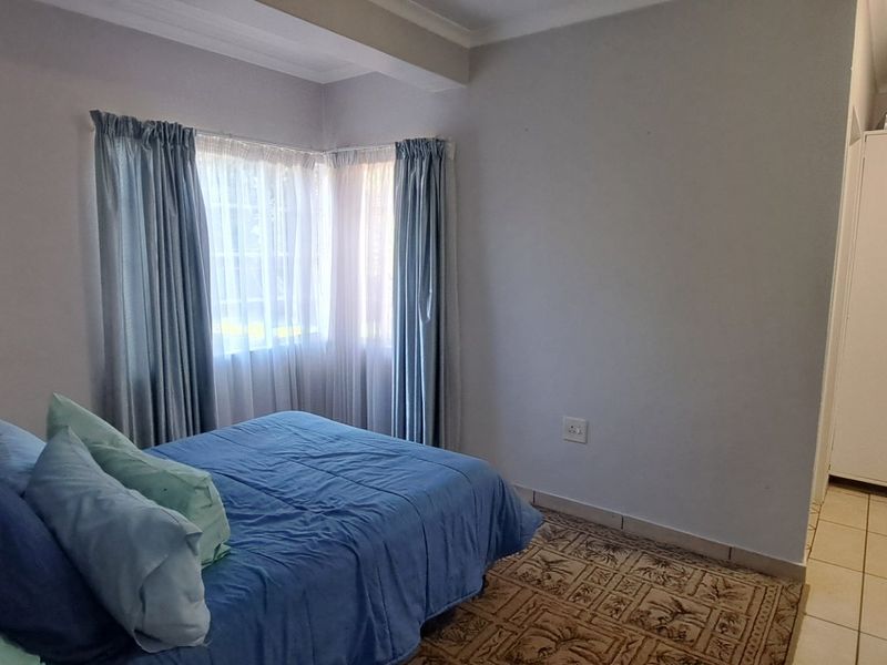 A functional bedroom featuring tiled flooring, a built-in cupboard, and corner windows that allow for natural light.