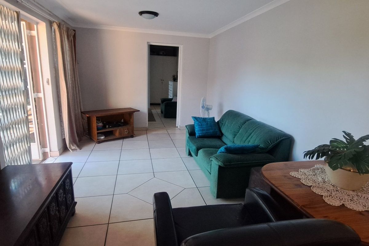 A living room featuring tiled flooring and a sliding glass door with a security gate, providing access to the outdoor area.