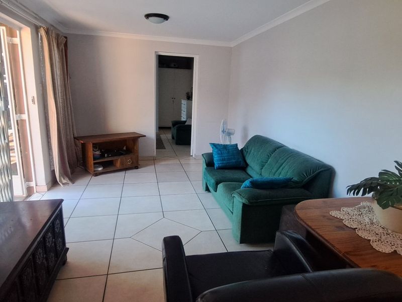 A living room featuring tiled flooring and a sliding glass door with a security gate, providing access to the outdoor area.