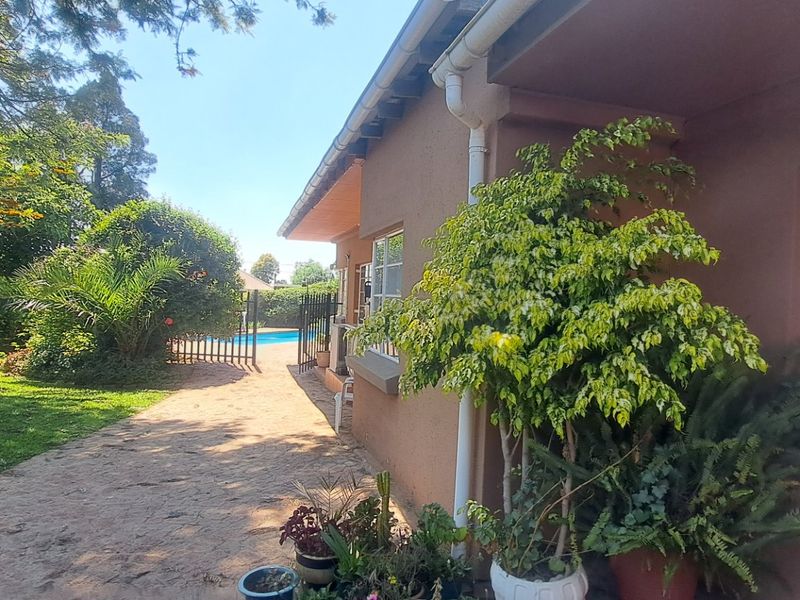 Rear exterior view of the property featuring a paved walkway, established garden, and a swimming pool enclosed by security fencing.