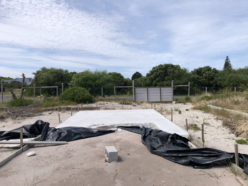 Vacant residential land featuring a partially completed concrete slab foundation, perimeter wire fencing, and natural sandy terrain.