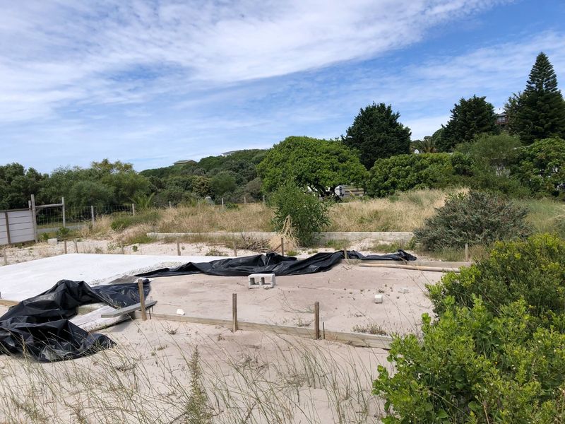 A vacant residential plot featuring a partially prepared concrete slab foundation and perimeter fencing, set within a natural coastal landscape.