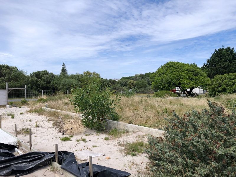 A vacant residential plot featuring sandy soil, partial concrete foundation work, and perimeter wire fencing, ready for development.