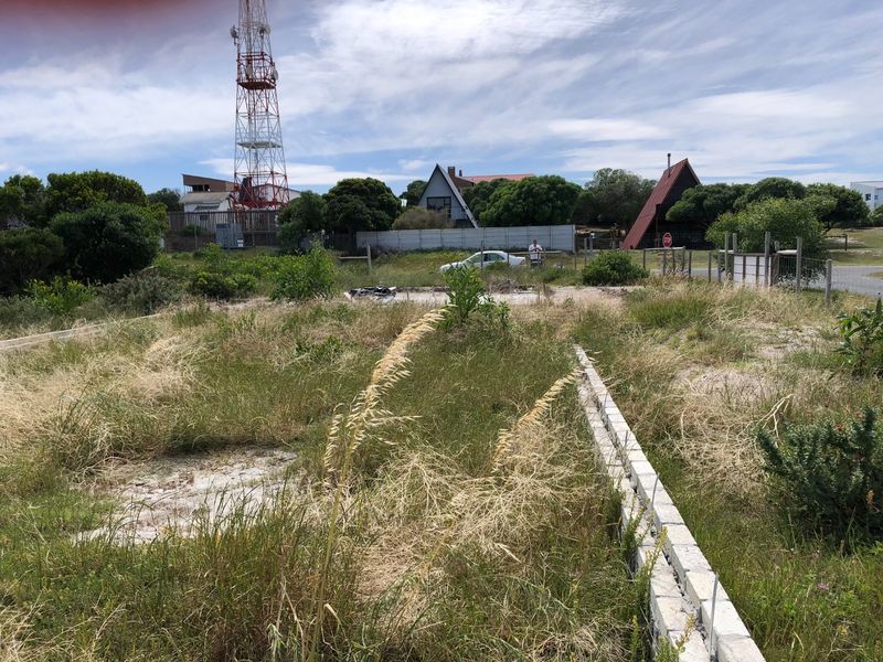 A vacant residential plot featuring overgrown grass and a partial concrete block boundary wall in a suburban setting.