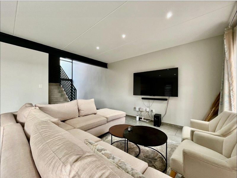 Modern living room featuring tiled flooring, recessed downlights, and an exposed structural steel beam, with an adjacent staircase and metal balustrade.