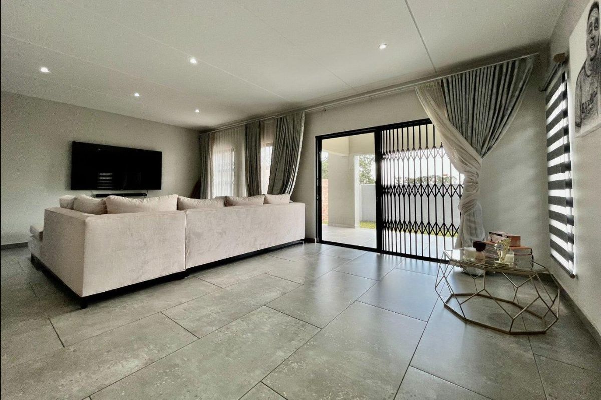 Spacious living room featuring large format floor tiles, recessed downlighting, and a sliding glass door with security gate leading to the patio.