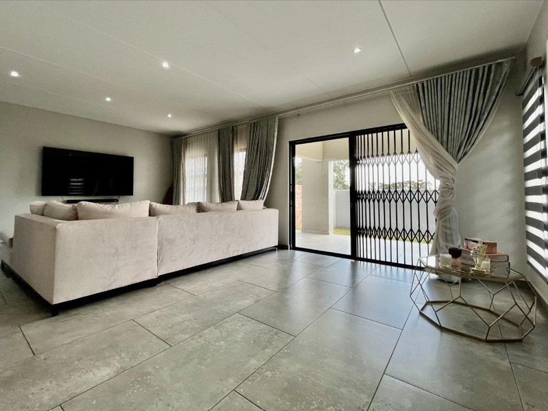 Spacious living room featuring large format floor tiles, recessed downlighting, and a sliding glass door with security gate leading to the patio.