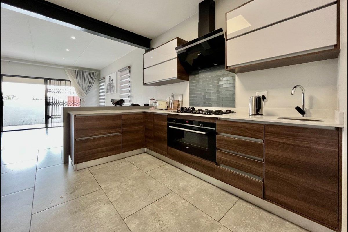 Modern kitchen featuring wood-grain cabinetry, stone countertops, gas hob, built-in oven, and a stylish subway tile backsplash, seamlessly integrated into an open-plan living space.
