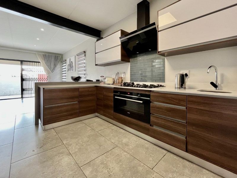Modern kitchen featuring wood-grain cabinetry, stone countertops, gas hob, built-in oven, and a stylish subway tile backsplash, seamlessly integrated into an open-plan living space.