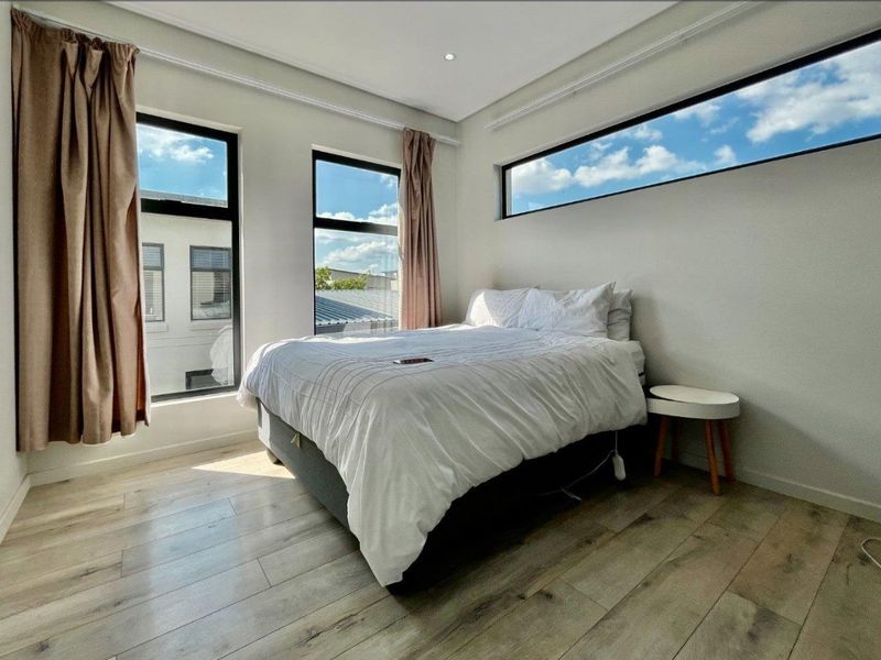 A bright and modern bedroom featuring light-toned laminate flooring, large windows, and a high-level clerestory window providing ample natural light.